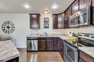 Kitchen with stainless steel appliances, dark wood finish cabinets, light countertops, and light wood-style flooring