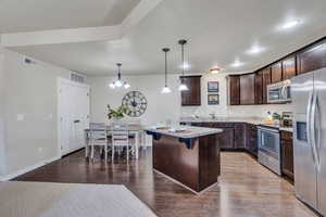 Kitchen with dark wood finish cabinetry, stainless steel appliances, a breakfast bar area, hanging light fixtures, and light wood-type flooring