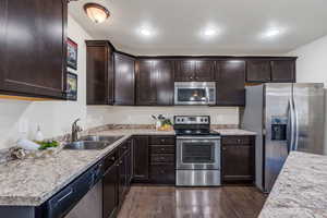Kitchen with stainless steel appliances, dark wood finish cabinetry, dark wood-style flooring, and light stone counters