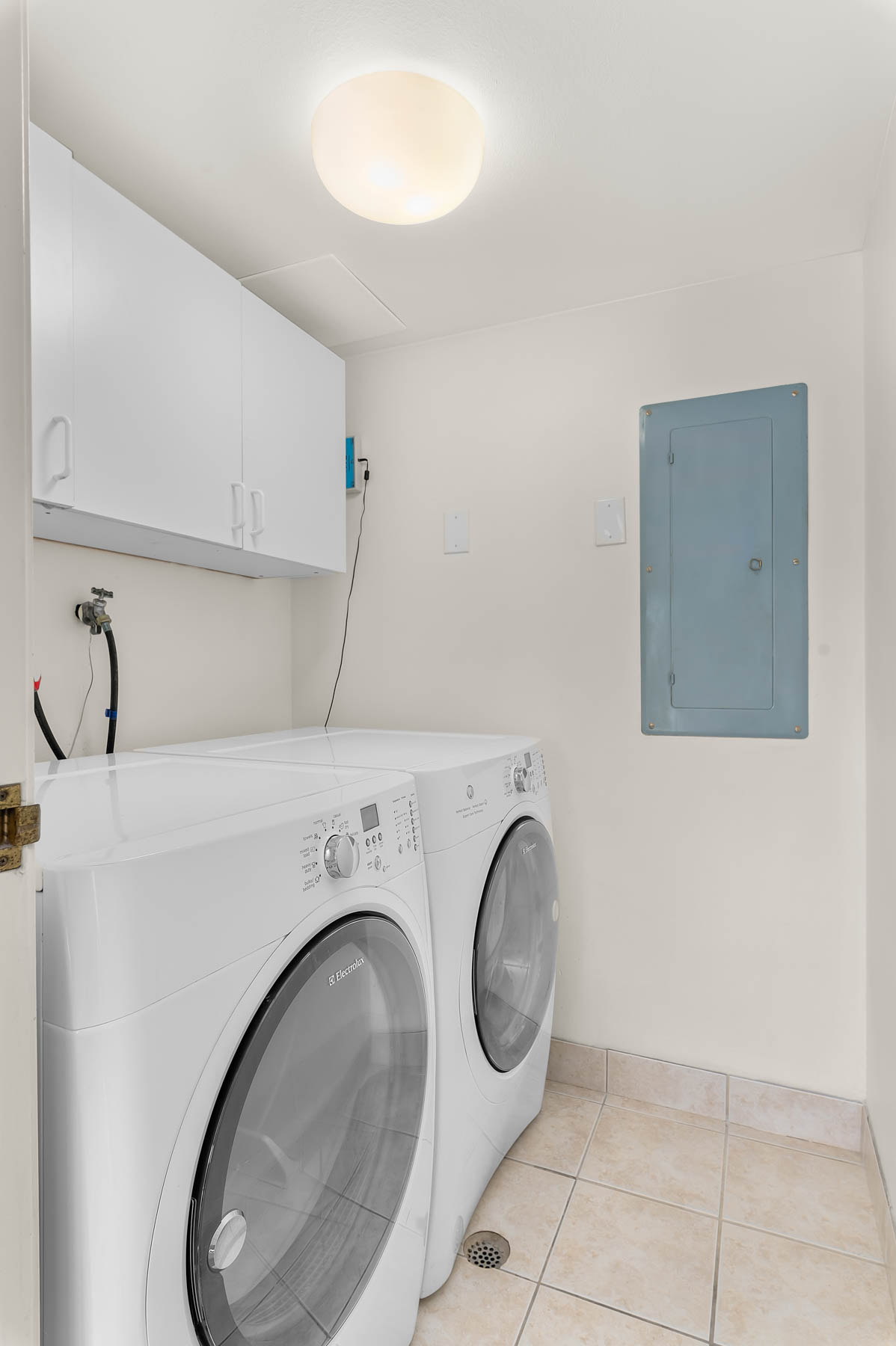 Laundry room with electric panel, washer and clothes dryer, cabinet space, and light tile patterned flooring