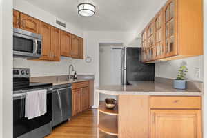Kitchen with stainless steel appliances, light stone counters, glass insert cabinets, light wood-type flooring, and wood finish cabinets