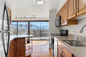 Kitchen with wood finish cabinets, stainless steel appliances, a mountain view, light wood-type flooring, and light stone counters