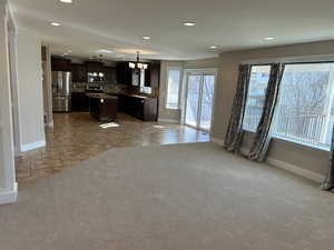 Kitchen featuring a kitchen island, open floor plan, dark wood finish cabinets, and light colored carpet