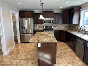 Kitchen with dark wood finish cabinets, stainless steel appliances, light stone counters, and a center island