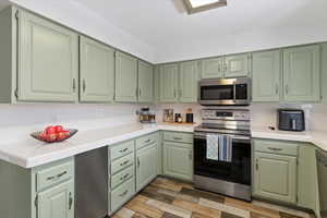 Kitchen featuring green cabinetry, stainless steel appliances, tile countertops, tasteful backsplash, and light wood finished floors