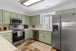 Kitchen featuring tile countertops, green cabinetry, stainless steel appliances, light wood-style floors, and backsplash