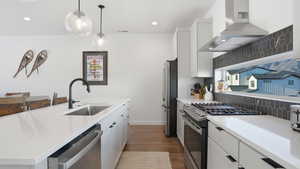 Kitchen with stainless steel appliances, a center island with sink, light wood finished floors, and white cabinetry