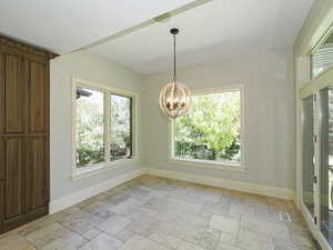 Unfurnished dining area with stone tile flooring and suspended lighting