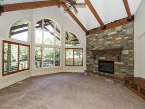 Unfurnished living room with carpet floors, a stone fireplace, and ceiling fan