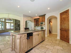 Kitchen featuring arched walkways, a breakfast bar, stone tile floors, recessed lighting, and stainless steel appliances