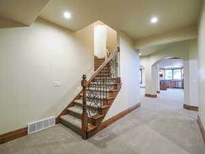 Stairs featuring arched walkways, carpet floors, and recessed lighting