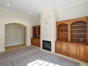 Unfurnished living room featuring stone tile floors, ornamental molding, a large fireplace, arched walkways, and recessed lighting