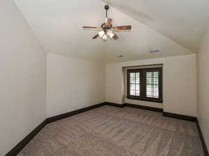 Unfurnished room featuring a ceiling fan, dark carpet, and lofted ceiling