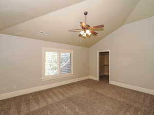 Spare room featuring dark colored carpet, ceiling fan, and vaulted ceiling