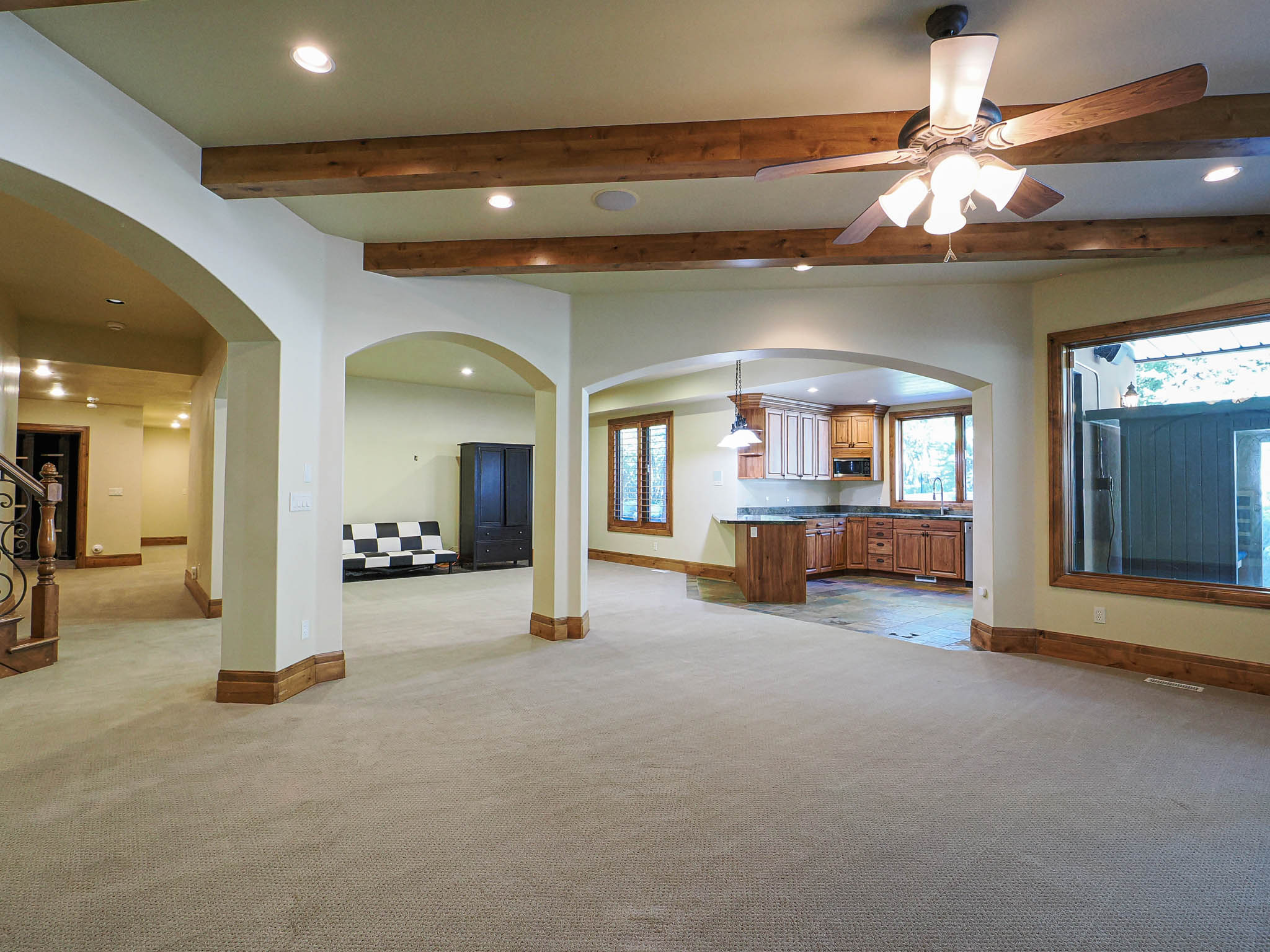 Unfurnished living room with arched walkways, recessed lighting, beamed ceiling, a ceiling fan, and light colored carpet
