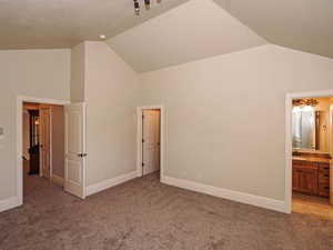 Unfurnished bedroom featuring connected bathroom, light colored carpet, and a high ceiling