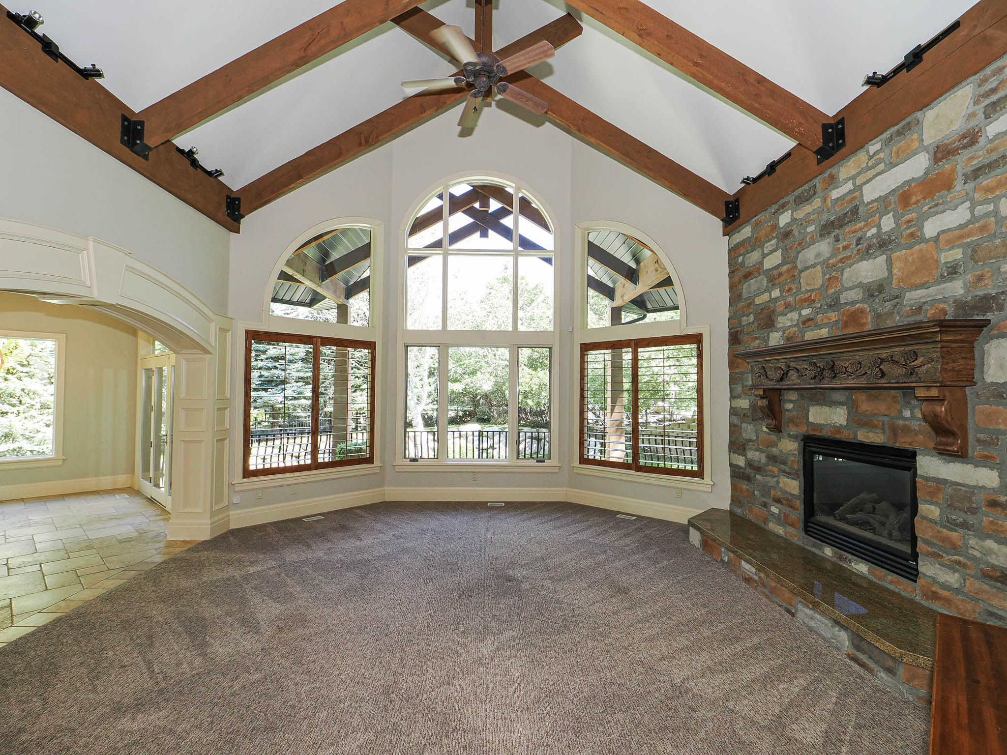 Unfurnished living room featuring a stone fireplace, carpet floors, stone tile floors, a ceiling fan, and plenty of natural light