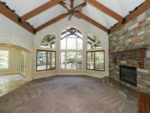 Unfurnished living room featuring a stone fireplace, carpet floors, stone tile floors, a ceiling fan, and plenty of natural light
