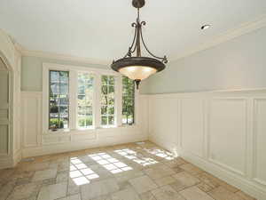 Unfurnished dining area with stone tile floors, ornamental molding, a decorative wall, and wainscoting