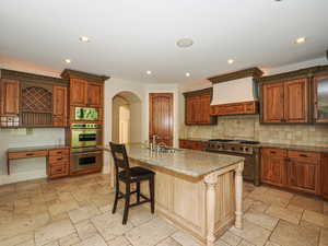 Kitchen with stone tile flooring, stainless steel appliances, arched walkways, recessed lighting, and a kitchen breakfast bar