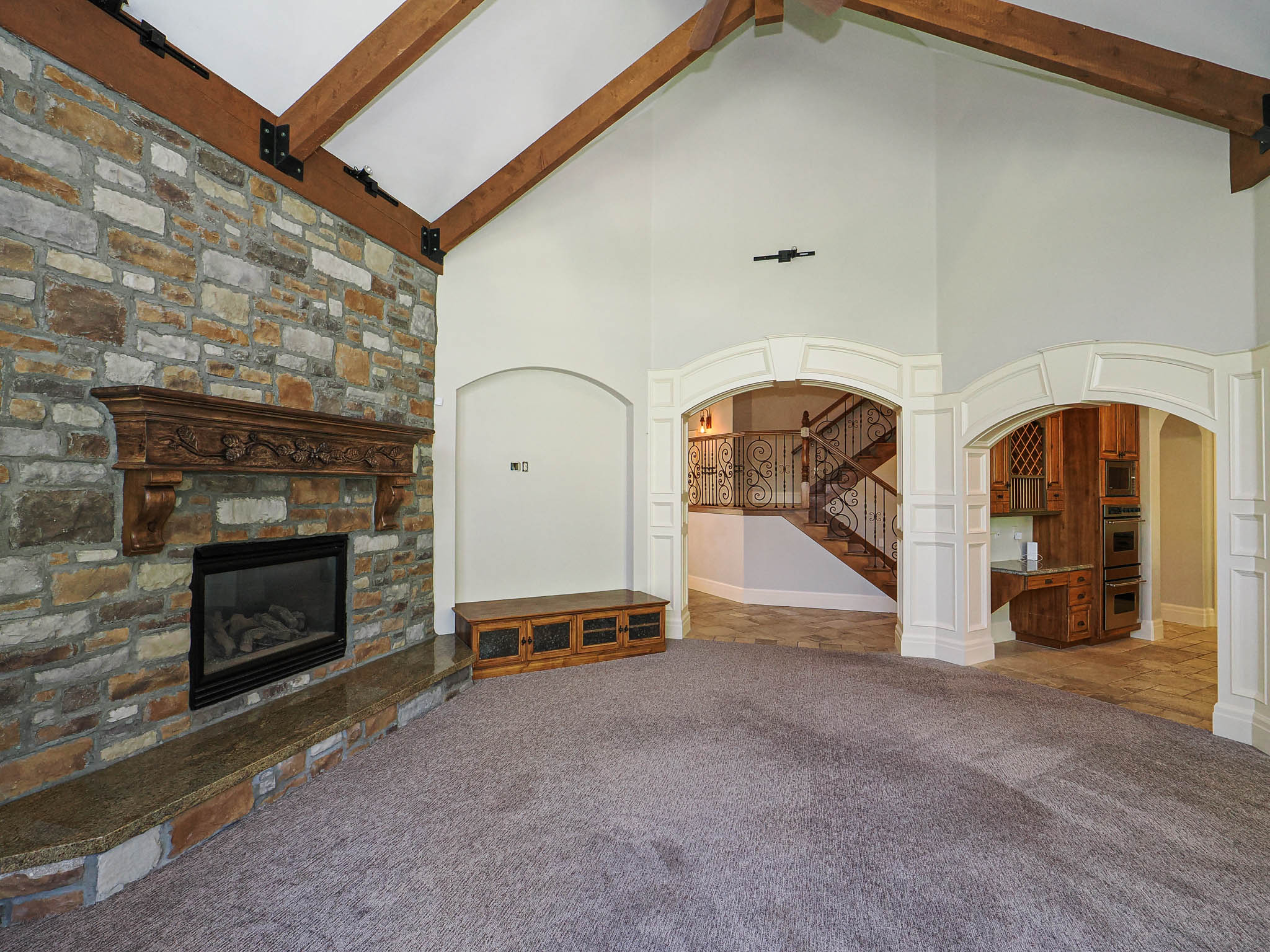 Unfurnished living room with arched walkways, carpet, and a stone fireplace