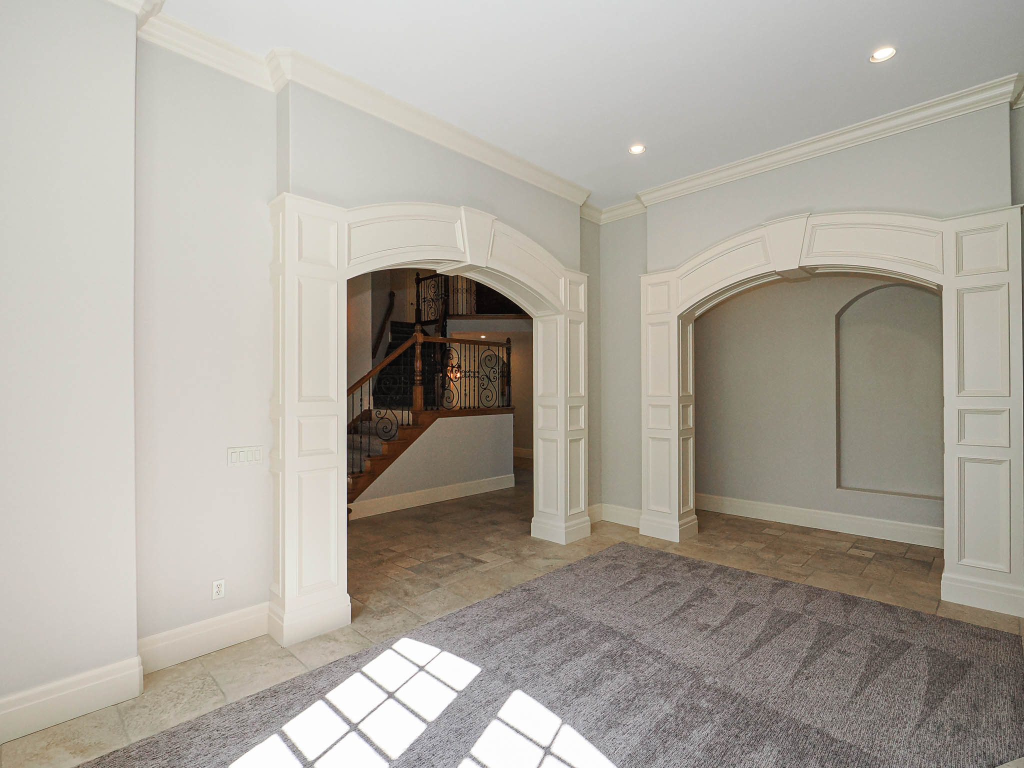 Empty room with arched walkways, stone tile flooring, and crown molding