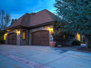 Property exterior at dusk with stone siding, concrete driveway, a shingled roof, and an attached garage