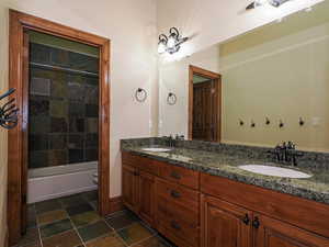Full bath with double vanity,  shower combination, and dark stone finish flooring
