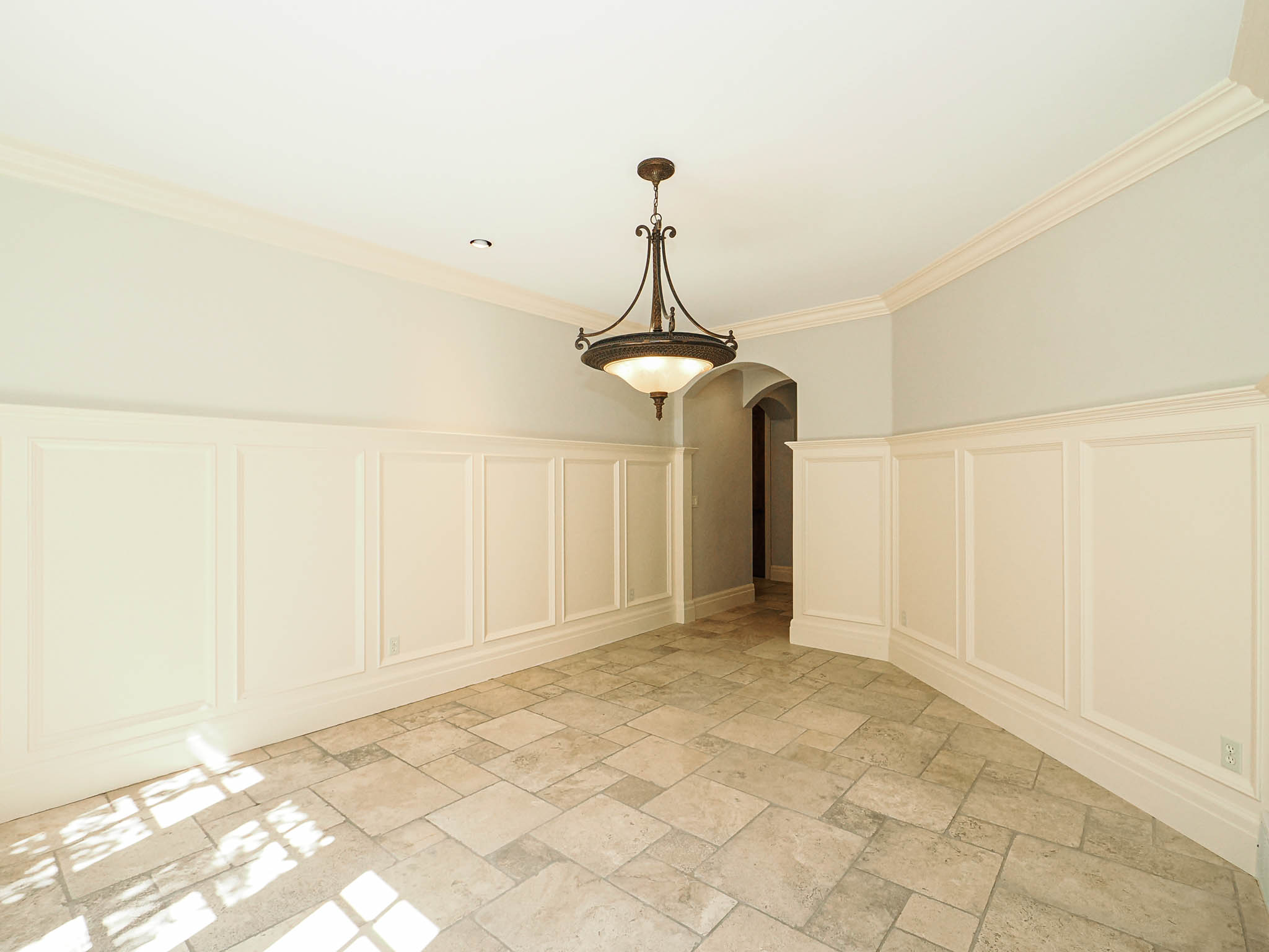 Unfurnished dining area featuring a decorative wall, a wainscoted wall, arched walkways, crown molding, and stone tile flooring