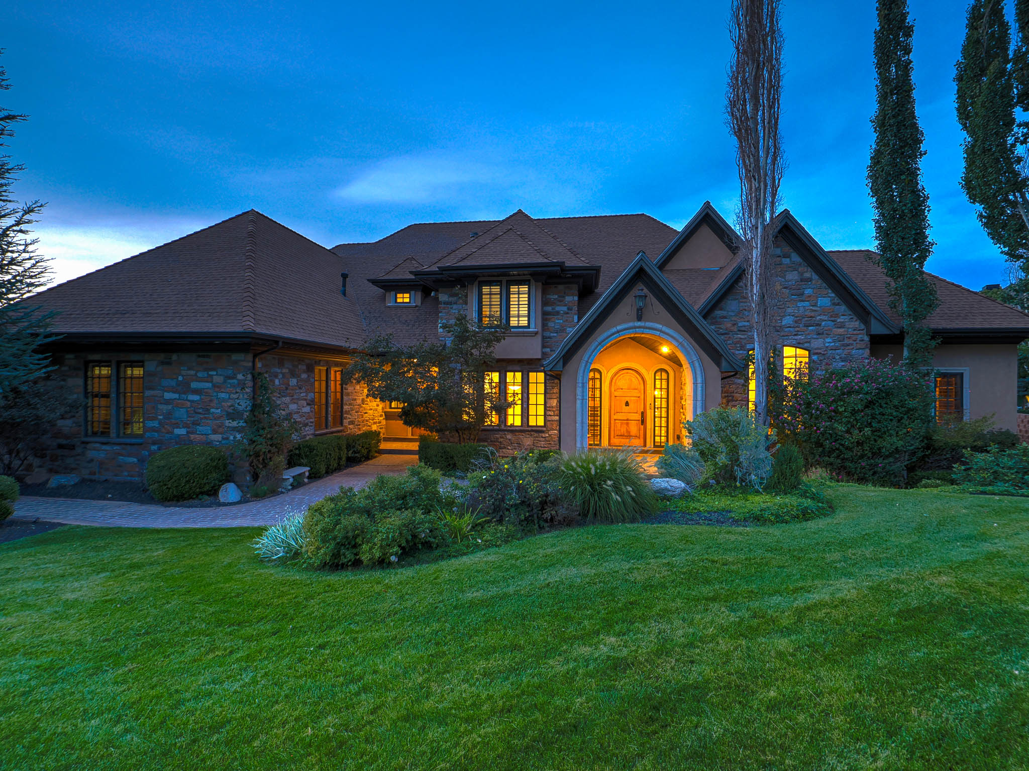 View of front of property with stone siding, a front yard, and roof with shingles