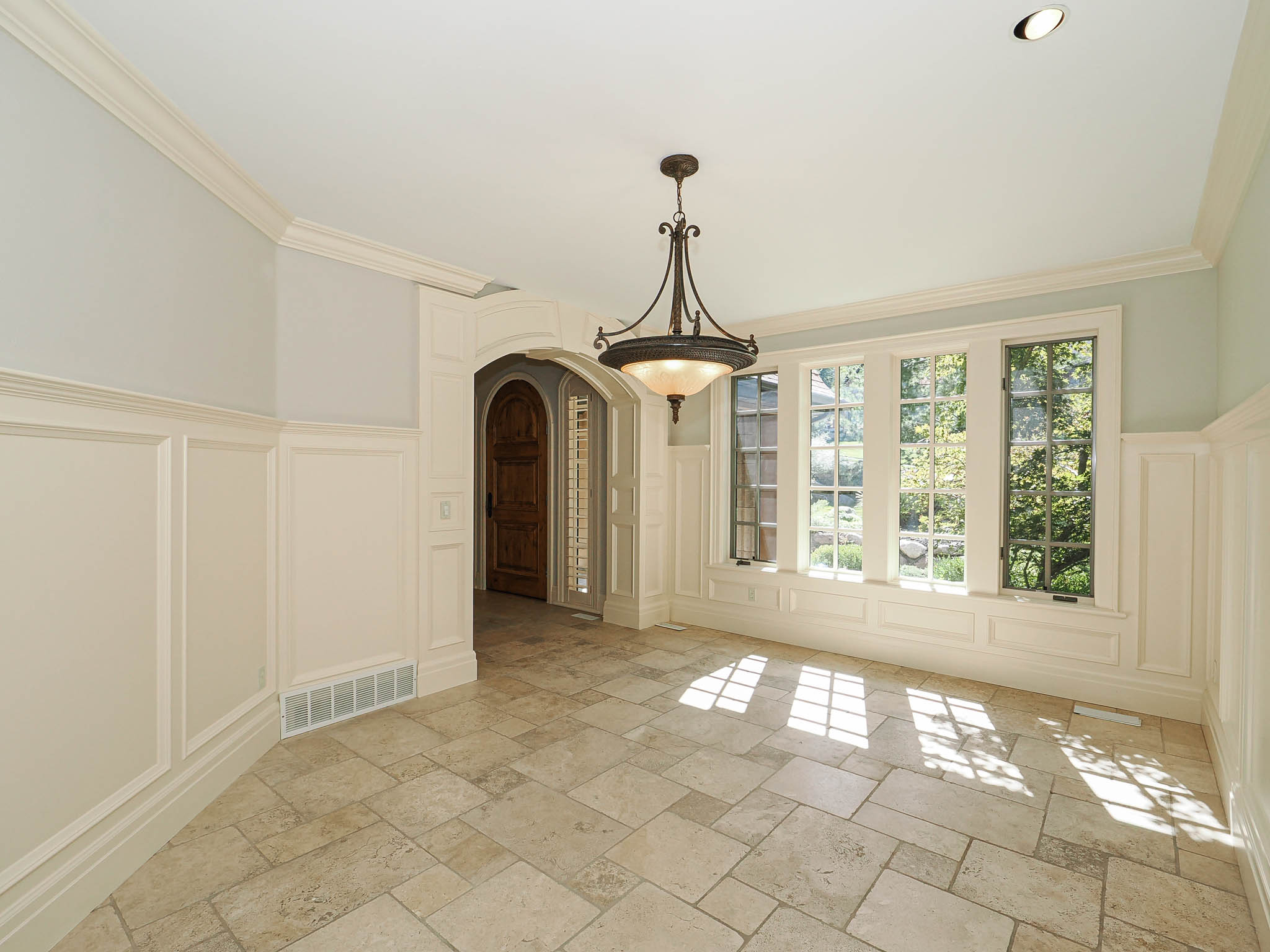 Unfurnished dining area with a decorative wall, arched walkways, wainscoting, stone tile flooring, and ornamental molding