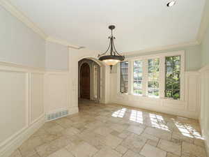 Unfurnished dining area with a decorative wall, arched walkways, wainscoting, stone tile flooring, and ornamental molding