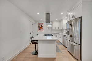 Kitchen featuring stainless steel appliances, white cabinetry, a breakfast bar, recessed lighting, and light wood-style floors