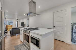 Kitchen with island exhaust hood, a kitchen island, stainless steel appliances, open floor plan, and white cabinets