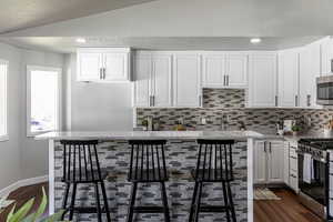 Kitchen with vaulted ceiling, white cabinets, stainless steel appliances, decorative backsplash, and light stone countertops