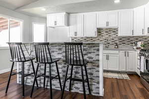 Kitchen with white cabinets, light stone counters, stainless steel range with gas cooktop, backsplash, and recessed lighting