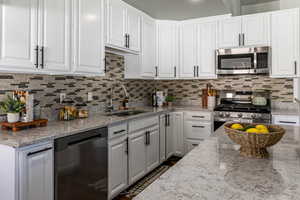 Kitchen with white cabinetry, stainless steel appliances, and light stone counters