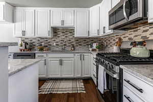 Kitchen with stainless steel appliances, white cabinets, light stone counters, and a textured ceiling