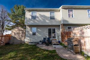 Back of house with a fenced backyard, a storage shed, and a patio area