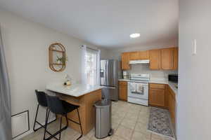 Kitchen featuring light countertops, white electric stove, stainless steel refrigerator with ice dispenser, a breakfast bar area, and a peninsula