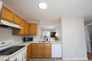 Kitchen with white appliances, light countertops, and wood finish cabinets