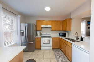 Kitchen featuring white appliances, wood finish cabinetry, light stone countertops, and light tile patterned flooring