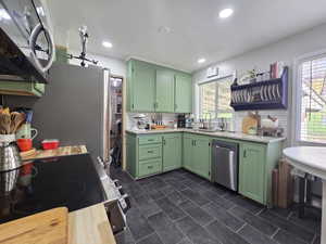 Kitchen featuring green cabinets, stainless steel appliances, decorative backsplash, and light stone counters