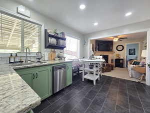 Kitchen with ceiling fan, light stone countertops, stainless steel dishwasher, decorative backsplash, and a fireplace