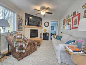 Living room featuring a fireplace, ceiling fan, a textured ceiling, and carpet floors