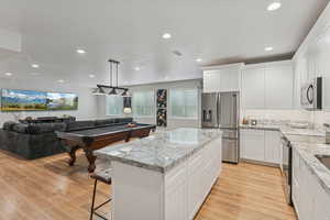 Kitchen featuring stainless steel appliances, light stone counters, a kitchen breakfast bar, a kitchen island, and white cabinets