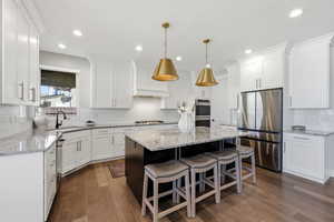 Two tone kitchen featuring a kitchen bar, light stone countertops, stainless steel appliances, a kitchen island, and dual tone cabinets