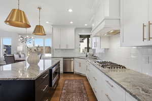 Dual tone kitchen with two tone cabinetry, light stone countertops, dark wood-style flooring, stainless steel appliances, and suspended lighting