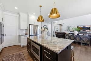 Two tone kitchen with two tone color scheme, light stone countertops, open floor plan, stainless steel appliances, and a center island