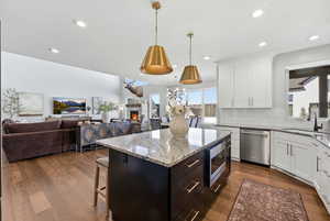 Kitchen with a breakfast bar, dark stone counters, two tone cabinets, stainless steel appliances, and dark wood-style floors